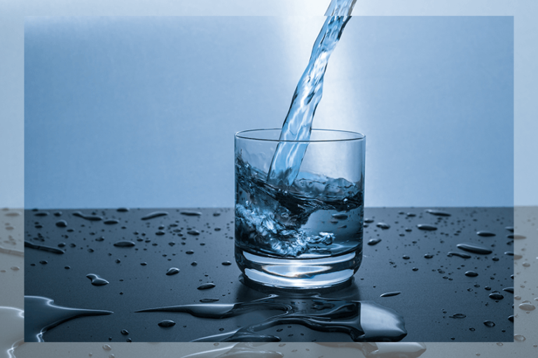 Wasser wird in ein Glas gegossen und der Tisch ist voll mit Wassertropfen